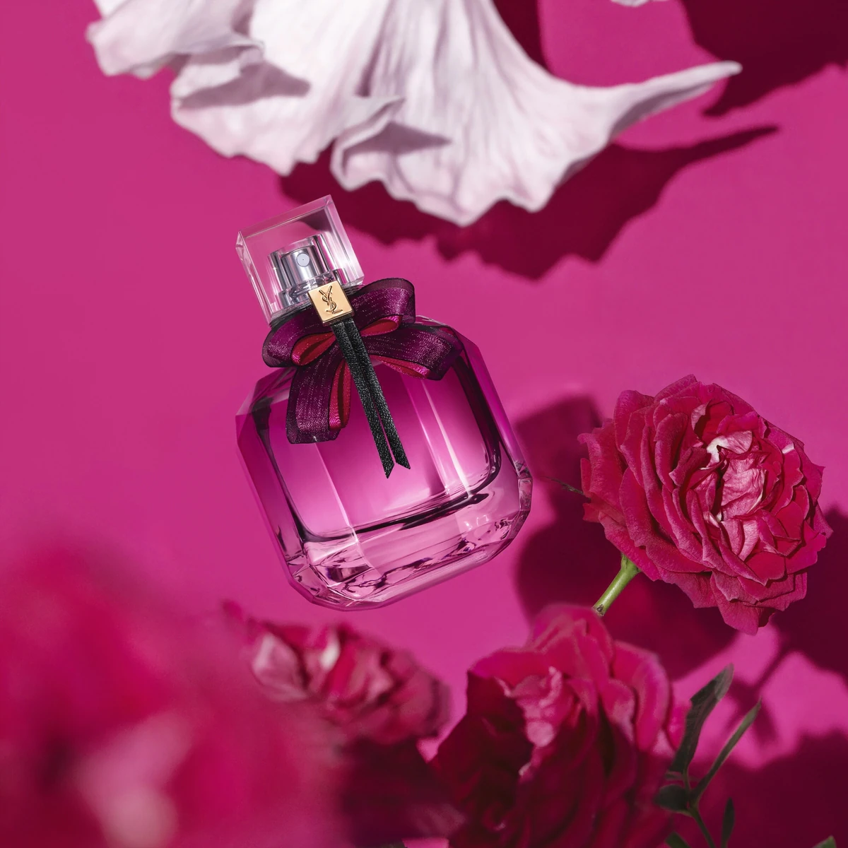 Yves saint laurent perfume. The boddle is pink with a transparent bottle cap including a bow around the cap. the background includes magenta roses with a magenta background. Photo credit: Shoppers Drug Mart